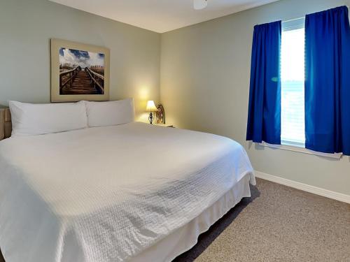 a bedroom with a large white bed with blue curtains at Grand Caribbean #306 West in Perdido Key