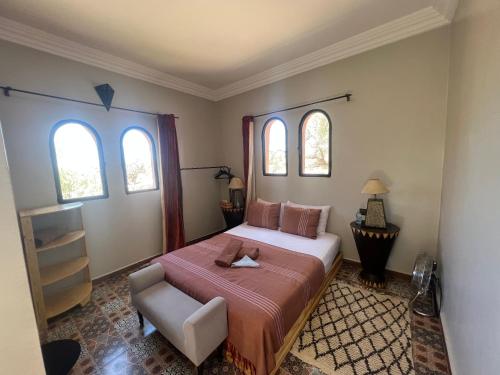um quarto com uma cama, uma cadeira e 2 janelas em Belle villa Baldi à la campagne d'Essaouira em Essaouira