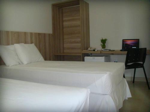 1 dormitorio con cama blanca y escritorio con ordenador en HOTEL TOPAZIO, en Cristalina