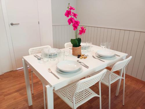By Urquinaona Rooms في برشلونة: طاولة بيضاء مع كراسي وصحون و مزهرية مع الزهور