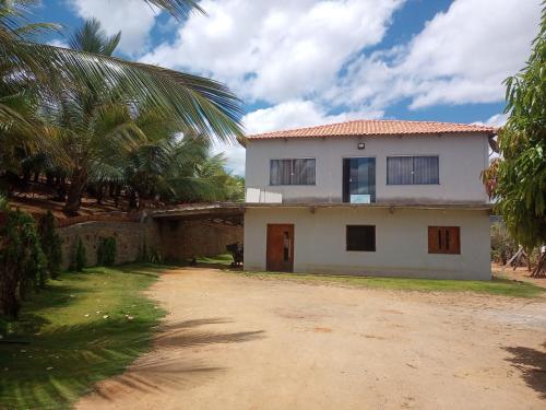 a white house with palm trees and a dirt road at Pousada e recanto baiano's in Amargosa