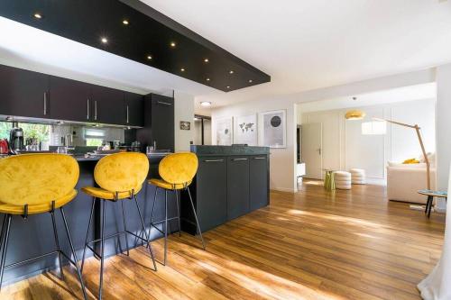 une cuisine avec des placards noirs et des tabourets de bar jaunes dans l'établissement Jardin Wilson, à Dijon