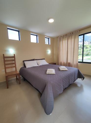 a bedroom with a large bed with a chair and windows at Villa Cosmopolita in Baños