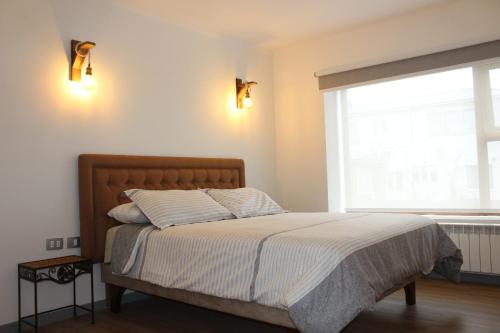 1 dormitorio con 1 cama con sábanas blancas y ventana en Hostal Alamo Patagonico, en Puerto Natales