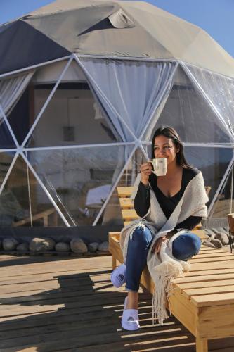 a woman sitting on a chair drinking a cup of coffee at Ecoglamping Tafí del Valle in Tafí del Valle