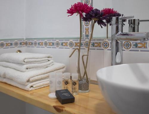 Un baño con toallas, un lavabo y un jarrón con flores. en Hostal Victoria, en Altura
