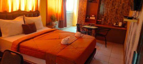 a hotel room with a bed with an orange comforter at Votel Hotel De'Pratnya Kediri in Kediri