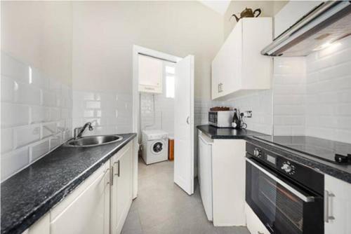 cocina blanca con fregadero y lavavajillas en Unique 1 BR flat btw Hammersmith & Fulham, en Londres