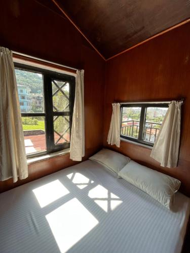 a bed in a small room with two windows at Bhaktapur Guest House in Bhaktapur