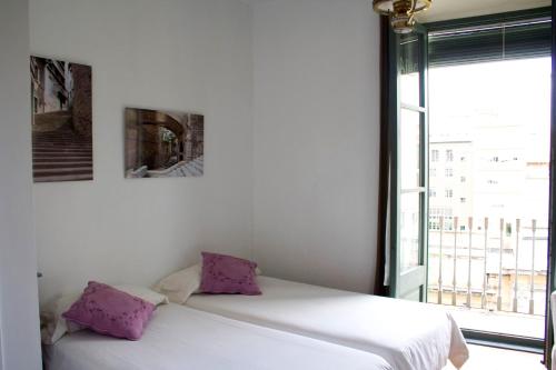 Cama blanca con almohadas moradas junto a una ventana en Bed & Breakfast Bells Oficis en Girona