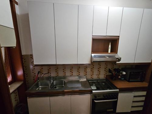 una cucina con armadi bianchi, lavandino e piano cottura di Ama's house a Piacenza