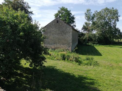 um velho celeiro de pedra num campo com árvores em Les chambres de balade au jardin em Épineu-le-Chevreuil