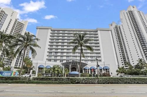 a large white building with palm trees in front of it at Ramada Marco Polo in Sunny Isles Beach