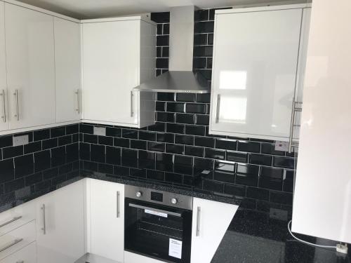 a kitchen with white cabinets and black tile on the wall at Brewery rd Double room in Plumstead