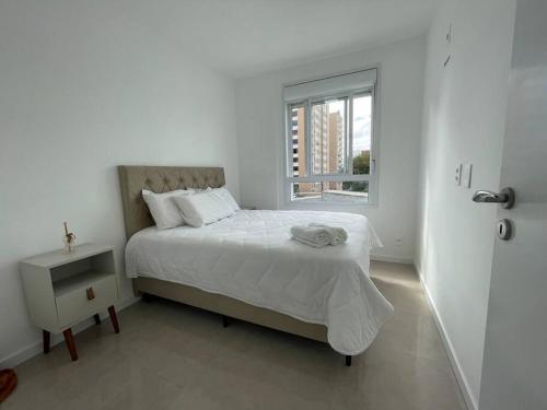 a white bedroom with a bed and a window at Apto Vilage Puc in Porto Alegre