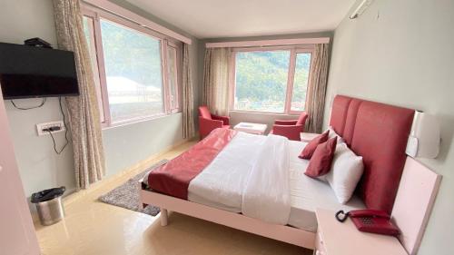 a bedroom with a bed with a red headboard and two windows at Hotel Mountain Meadows in Manāli
