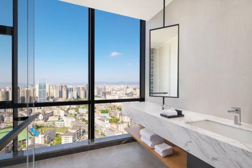Fairfield by Marriott Kunming Xinying في كونمينغ: حمام مع حوض ونوافذ كبيرة