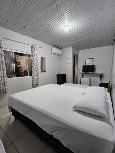 a large white bed in a room with a window at Aconchego Lar Cama e Café in Foz do Iguaçu