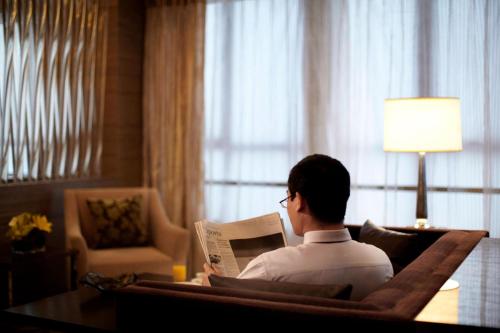 a man sitting in a chair reading a newspaper at Courtyard by Marriott Kunshan in Kunshan