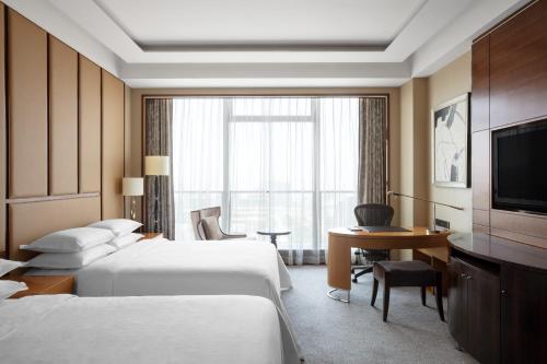 Habitación de hotel con 2 camas, escritorio y TV. en Sheraton Qingdao Jiaozhou Hotel, en Jiaoxian