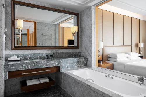 een badkamer met een bad, een spiegel en een bed bij Sheraton Qingdao Jiaozhou Hotel in Jiaozhou
