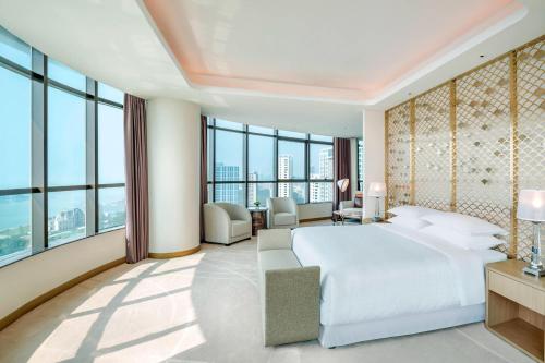 sypialnia z białym łóżkiem i dużymi oknami w obiekcie Sheraton Qingdao West Coast w mieście Huangdao
