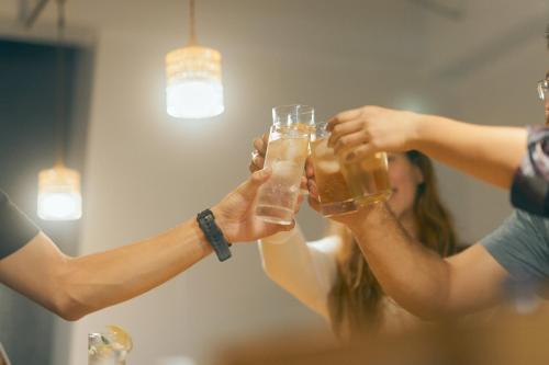 two people holding glasses of beer in front of a mirror at Common de - Hostel & Bar in Fukuoka