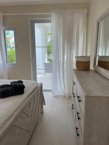a white bedroom with a bed and a large window at Fully renovated Beachfront 1BR Condo in the gated Stanza Mare community with a private beach, pool, onsite restaurant and modern amenities such as refrigerator, dishwasher, filtered water, microwave, BBQ, washer dryer, bamboo linens, free Wi-Fi in Punta Cana