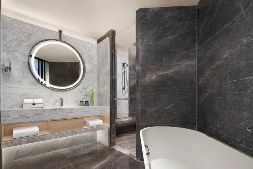 ein Bad mit einer Badewanne und einem Spiegel in der Unterkunft Liyang Marriott Hotel in Liyang