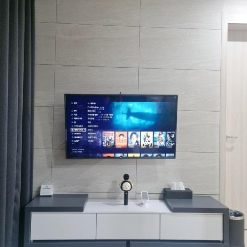 a tv on a wall with a desk with a clock at Yangyang Ocean Stay 환상적 전면 오션뷰 in Yangyang