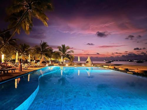 a swimming pool at a resort with a sunset at Angsana Velavaru in Dhaalu Atoll