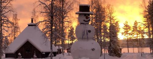 un muñeco de nieve frente a una casa en la nieve en Palojärven Lomakeskus en Sonka