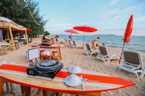 a surfboard on a beach with chairs and umbrellas at Bayphere Hotel Pattaya JC in Na Jomtien