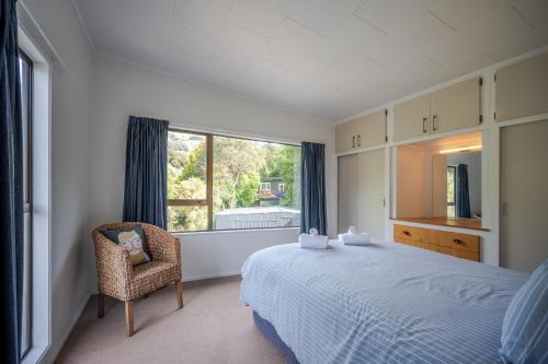 ein Schlafzimmer mit einem Bett, einem Stuhl und einem Fenster in der Unterkunft Bay View - Wainui Holiday Home in Akaroa