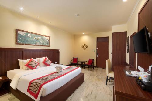 een slaapkamer met een bed, een bureau en een televisie bij Grand Istana Rama Hotel in Kuta