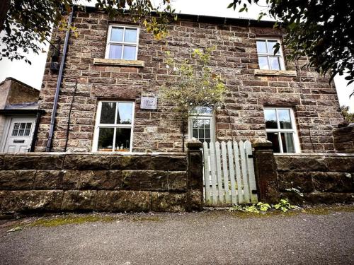 a brick building with a white fence in front of it at Luxurious cottage with cosy fireplace in Matlock in Winster