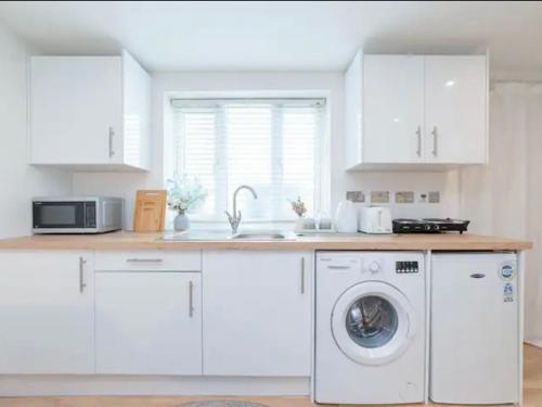 a kitchen with white cabinets and a washing machine at Pass the Keys Cozy Studio just 20 mins to Central London in Raynes Park