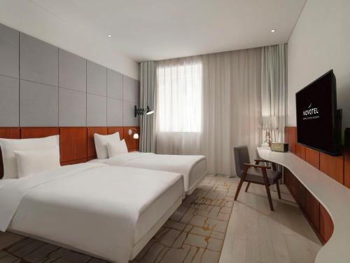 上海市にあるNovotel Shanghai Hongqiao Exhibitionのベッド2台、薄型テレビが備わるホテルルームです。