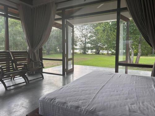 a bedroom with a bed and large glass windows at Magalle Wewa Villa in Nikaweratiya