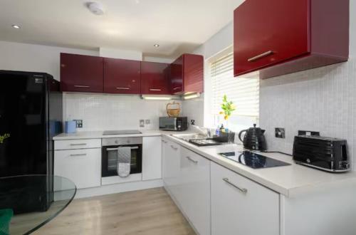 una cocina con encimeras blancas y armarios rojos en Modern 2 Bedroom Flat with Parking in Cardiff, en Cardiff