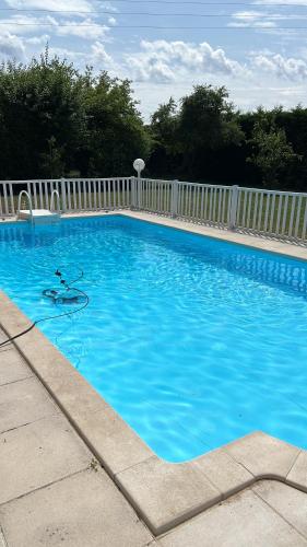 une grande piscine bleue à côté d'une clôture blanche dans l'établissement La Maillardière - Maison de campagne avec piscine, à Corné