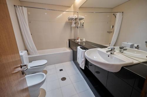 a bathroom with a sink and a toilet and a tub at Hotel Praia Marina by RIDAN Hotels in Praia da Vitória