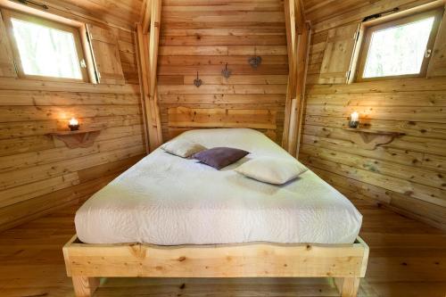 a bed in a log cabin with two windows at Les Cabanes de Fontfroide in Saint-Antoine