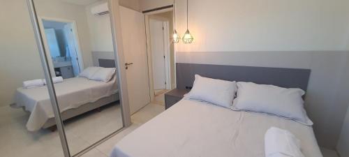 a bedroom with a mirror and a bed with white pillows at Apartamento 2 suítes 200m da praia de Bombas in Bombas