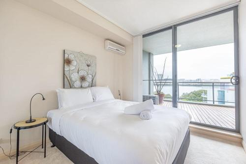 a bedroom with a large white bed and a large window at Cozy 2BD Apt w Waterview near Olympic Park in Sydney