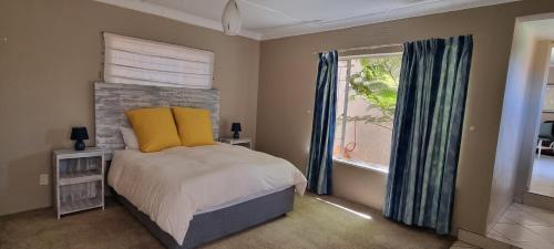 a bedroom with a bed with yellow pillows and a window at Cottage on Kei in Germiston