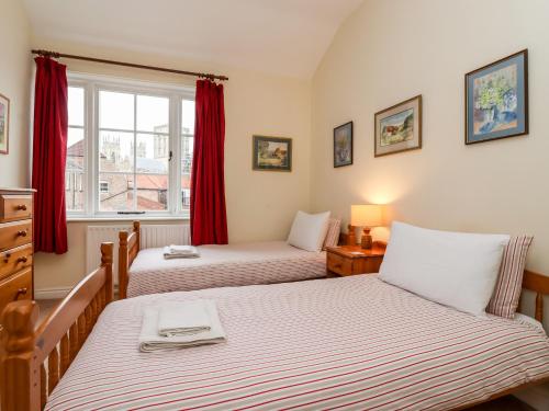 two beds in a bedroom with red curtains and a window at 6 Granary Court in York