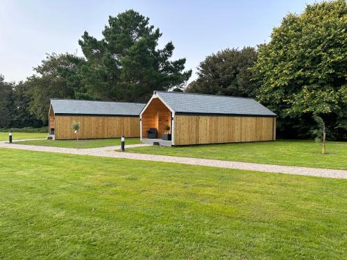 a large wooden building in a field with trees at Riverside Retreats - Steamers Meadow in Gwinear