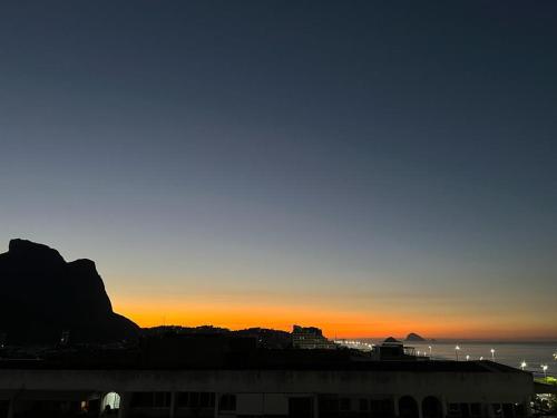 a sunset over a city with a mountain in the background at Vista para o mar Barra da tijuca in Rio de Janeiro