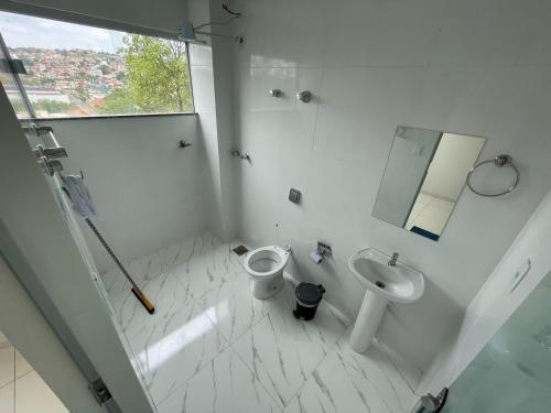 a white bathroom with a toilet and a sink at Shalom Flat Hotel in Pará de Minas